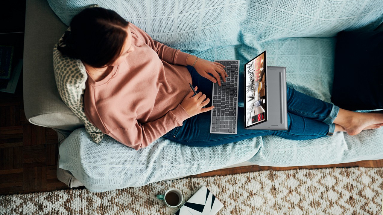 Person using a Dell Plus laptop while lying comfortably on a sofa