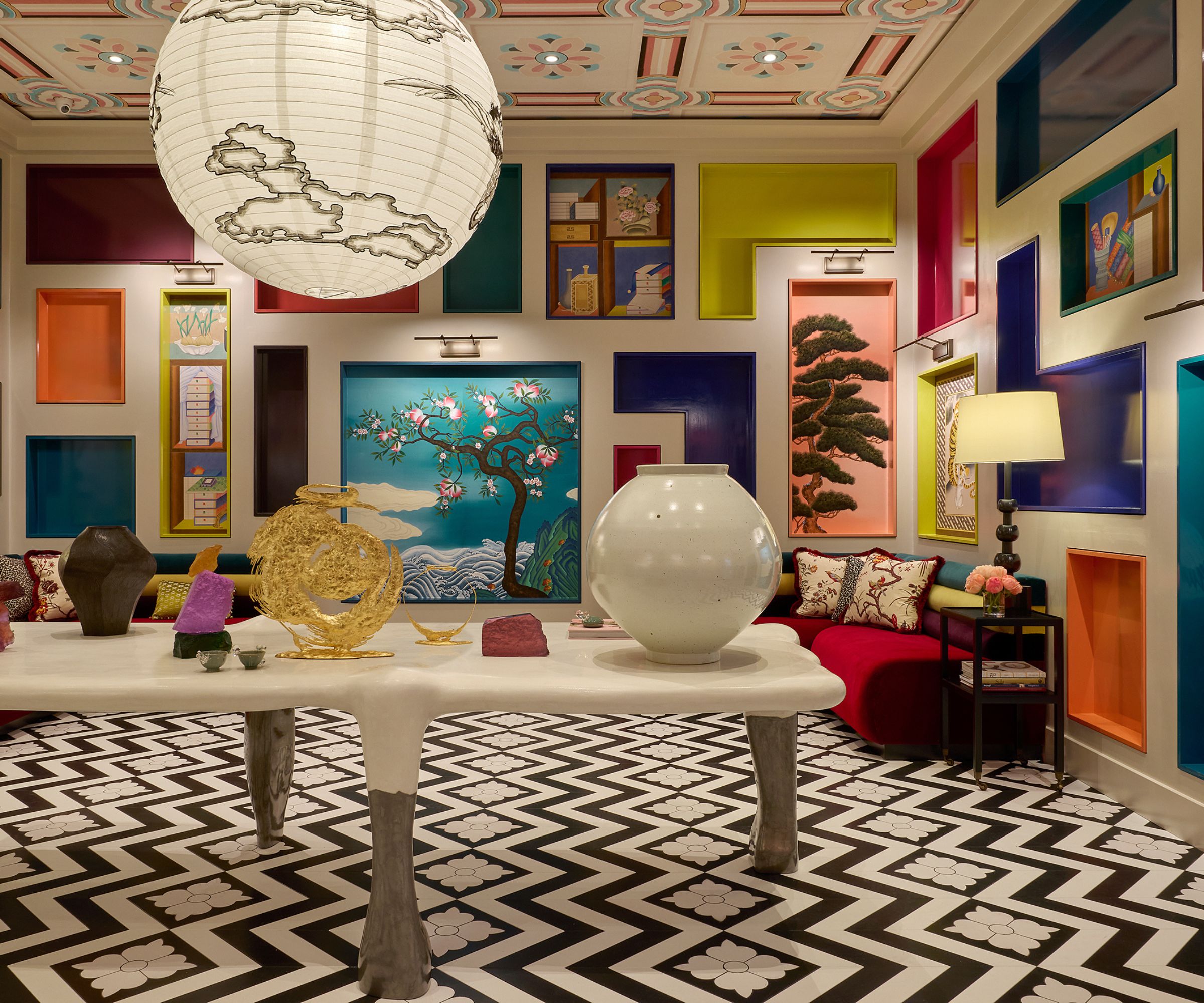 Lobby room with black and white floor, long white table with ceramics and art on top, and mural walls with colourful lacquer installations