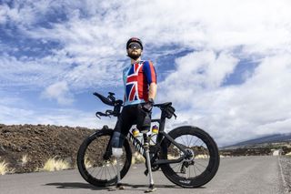 A posed shot of Billy by his bike, against an expansive background and a sunny, blue and white cloudy sky.