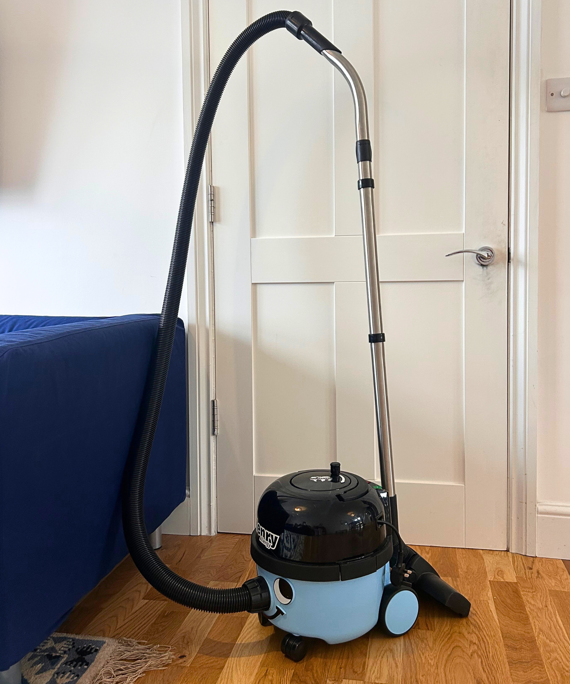 Megan's Henry Allergy vacuum cleaner on wooden flooring in front of a white door with the corner of a blue sofa in the left