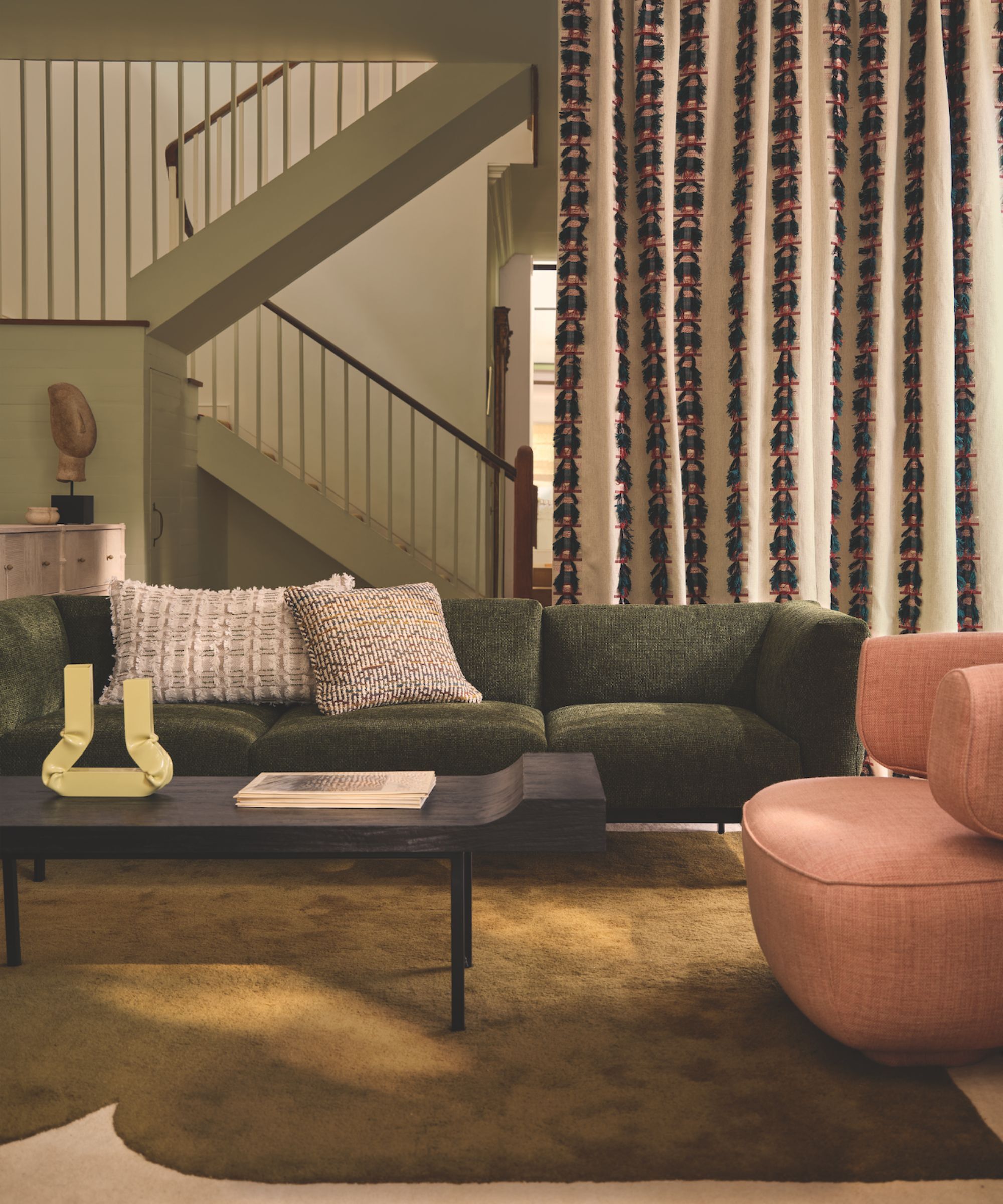 Living room with multiple colours and textures, a green sofa, pile rug, pink chair and a large floor length patterned curtain