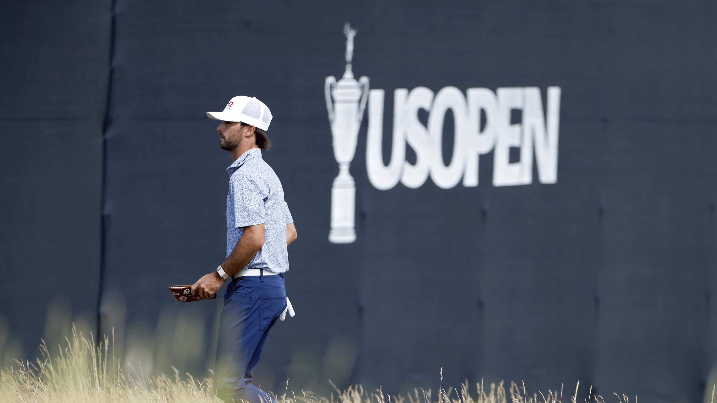 Ryder Cowan walks past a US Open sign at Shinnecock Hills in 2026