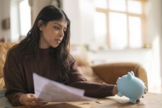 A woman looks at her piggy bank as she ponders the effect of the last interest rate cut on her savings (image: Getty Images)