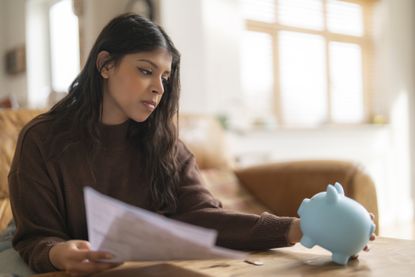 A woman looks at her piggy bank as she ponders interest rate cuts for her savings (image: Getty Images)