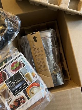 Unboxing the Ninja Detect Duo Power Blender, open box pictured from above shows attachments wrapped in clear plastic and a recipe book with 10 easy, quick ideas
