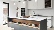 A modern kitchen with grey and wooden island with open shelving, and white handleless cabinetry