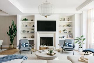 A neutral living room with symmetrical alcove bookshelves and blue upholstery accents