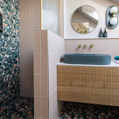 Bathroom with pink shower area and wooden ribbed storage cabinet.