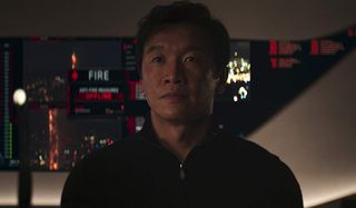 Skyscraper Chin Han stands in front of an important control panel.