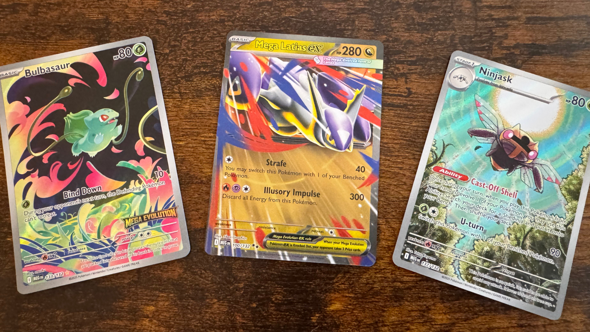 Three Pokemon TCG Mega Evolution cards laid out on a wooden surface