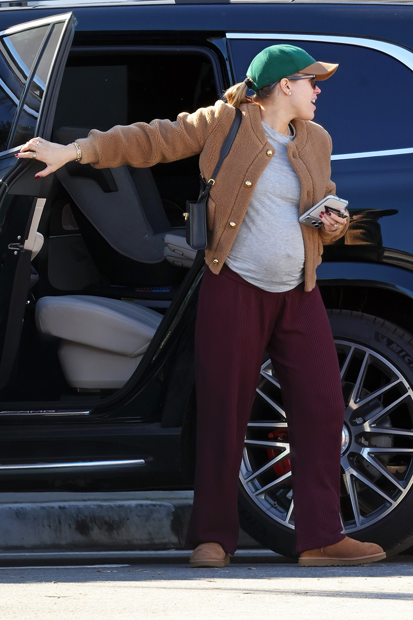 Sofia Richie wearing a camel jacket, gray T-shirt, burgundy pants, a baseball cap, and Uggs