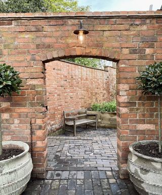 A brick patio archway with a bracket light fitting