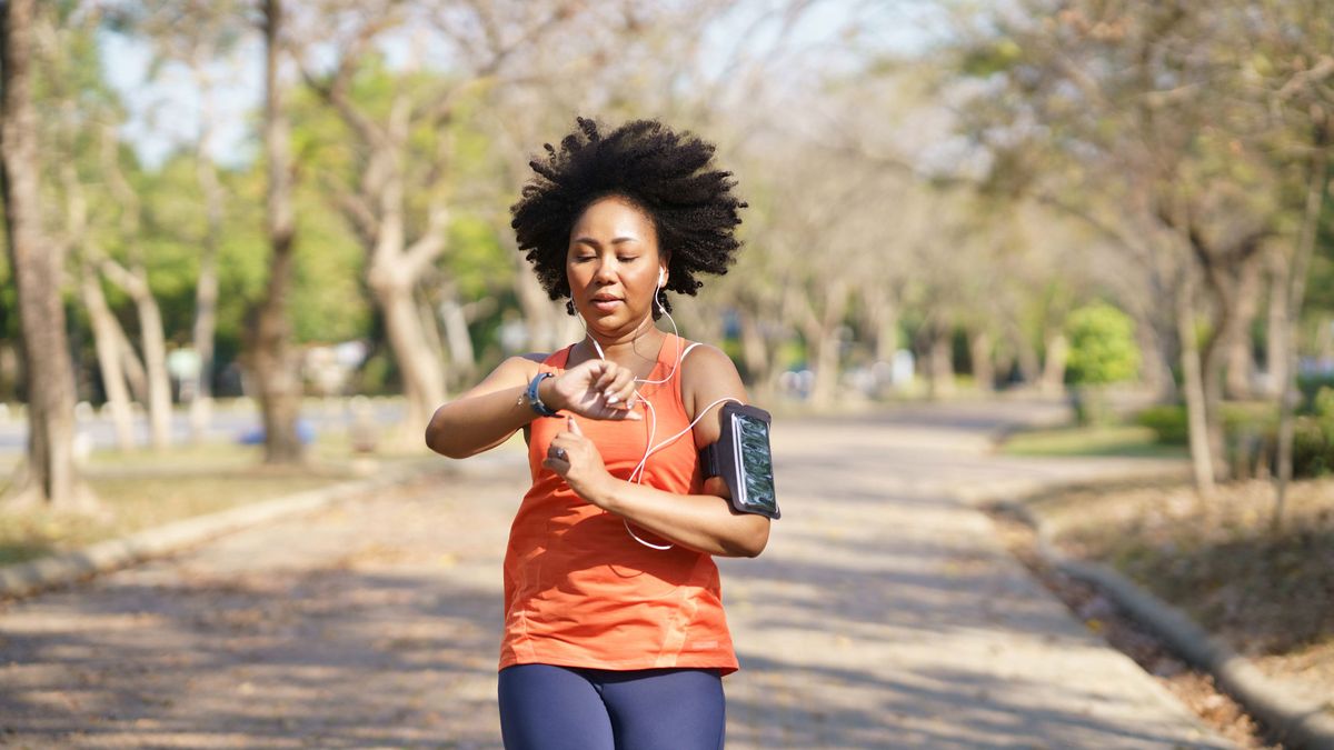 A woman jogging in a park is checking her running watch