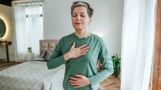 Woman with hand on stomach and hand on chest, practising Kegel exercises at home