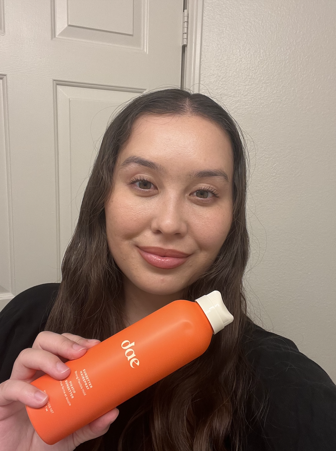 girl with dark brown hair standing in her bathroom and holding up a can of orange dae hairspray