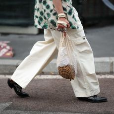 guest wears a beige with green leaves print pattern short sleeves shirt, a black shiny leather nailed / studded belt, pale yellow large cargo pants, a white latte mesh cotton handbag, black shiny leather with white embroidered seams shoes, silver rings , outside JW Anderson, during the Milan Fashion Week - Menswear Spring/Summer 2024 on June 18, 2023 in Milan, Italy. (Photo by Edward Berthelot/Getty Images)