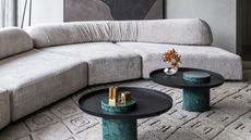gray sofa, gray patterned rug, two black side tables with green marble base, gray walls with artwork behind sofa