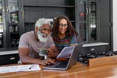 A retired couple is smiling as they work on a laptop to determine their budget.