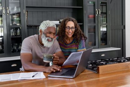 A retired couple is smiling as they work on a laptop to determine their budget.