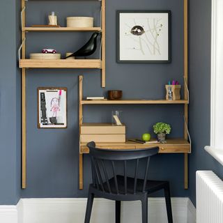 a small home office in an alcove with grey blue walls, wooden foldable shelving and a black chair