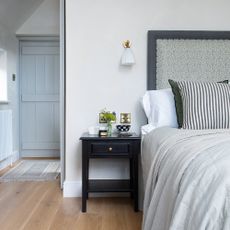 A bedroom with an upholstered headboard, wooden flooring, and a striped black and white cushion on the bed