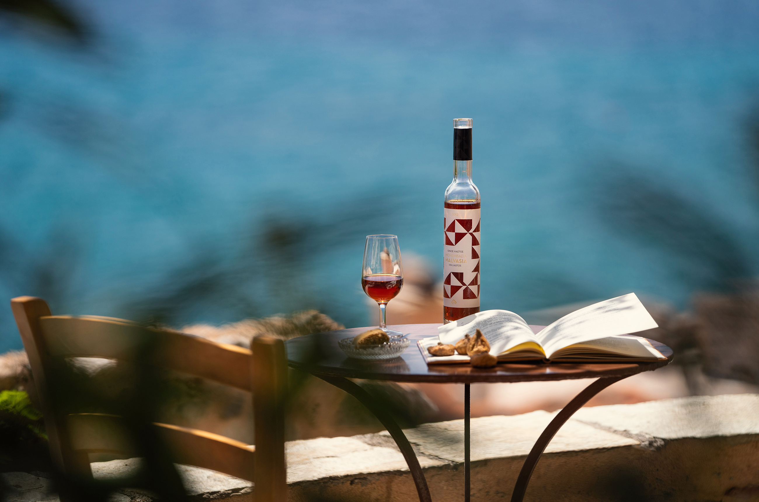 A wine bottle and glass on a table in front of sea