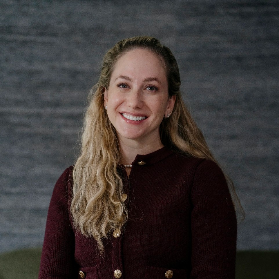 A woman with long blonde curly hair, Tehilla Bennet, poses for a headshot.