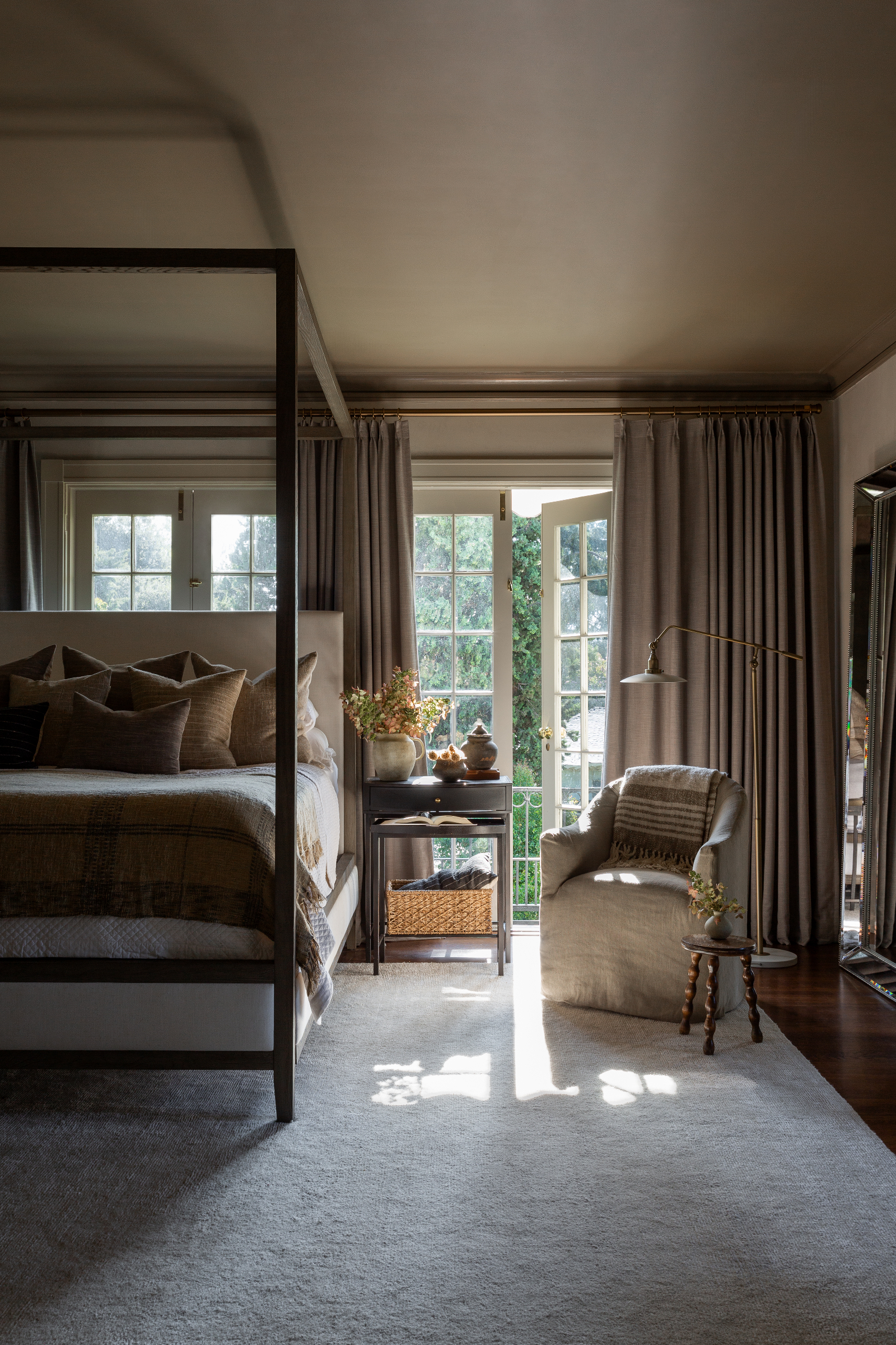 Calm smart bedroom with layered neutral tones, four poster bed, curtains, armchair, large cream rug and patio doors