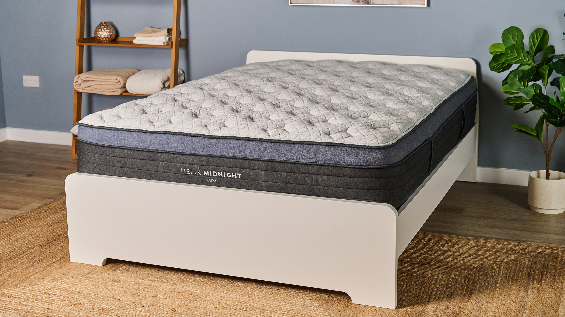 The Helix Midnight Luxe mattress placed on a white wooden bedframe, photographed in our blue coloured Testing Lab
