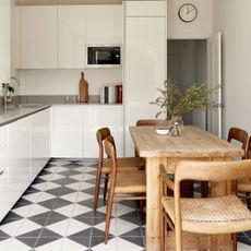 White kitchen with gloss cabinets, wooden dining table and chairs and black and white floor tiles
