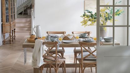 A dinig room with light wooden table and four matching chairs, laid out with white dinnerware