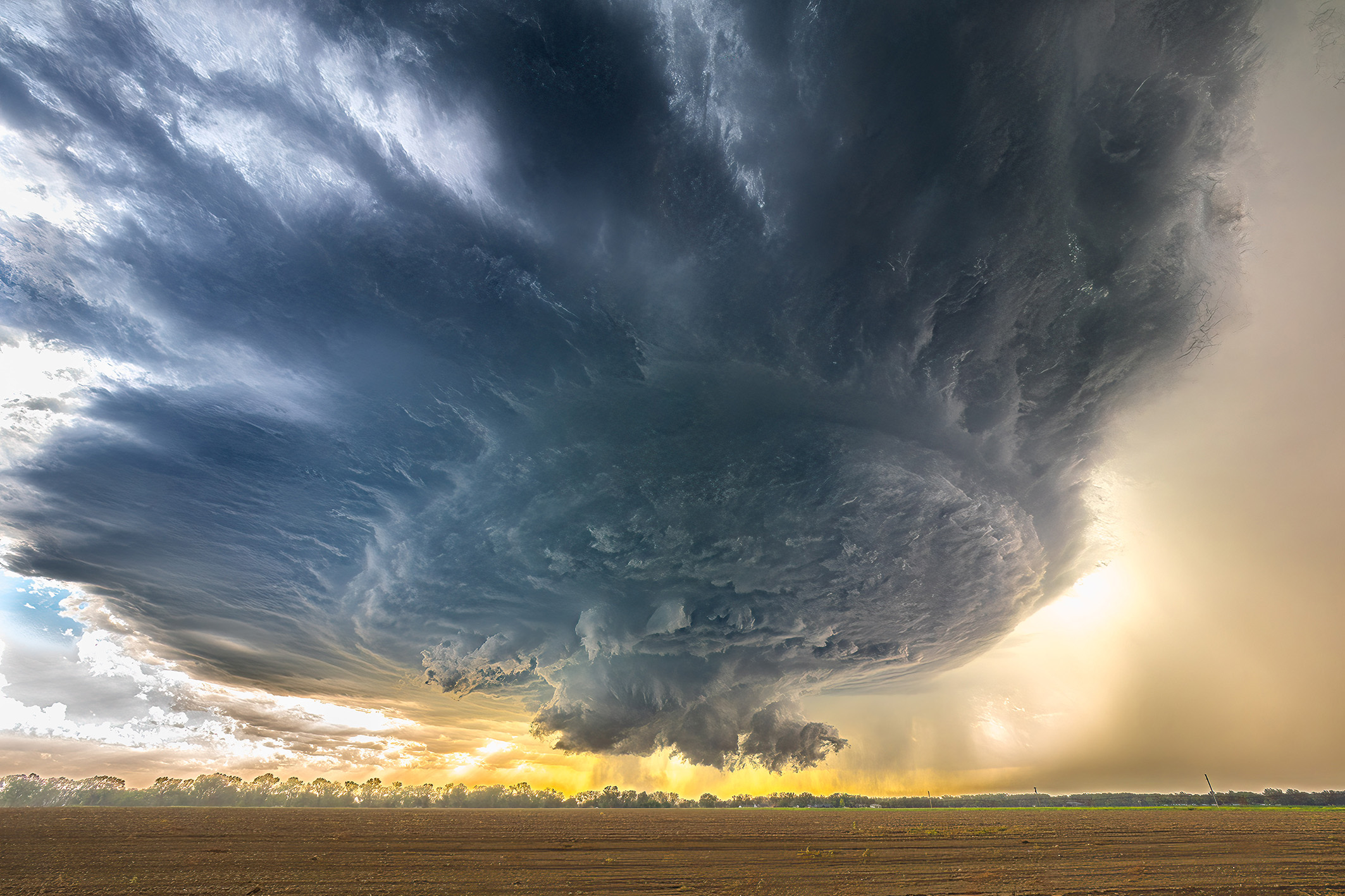 A dramatic swirling storm cloud looms over a plain, illuminated by a golden sunset, creating a striking contrast between dark and light
