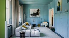 Blue living room with pale blue chaise sofa, black glass side tables and abstract artwork