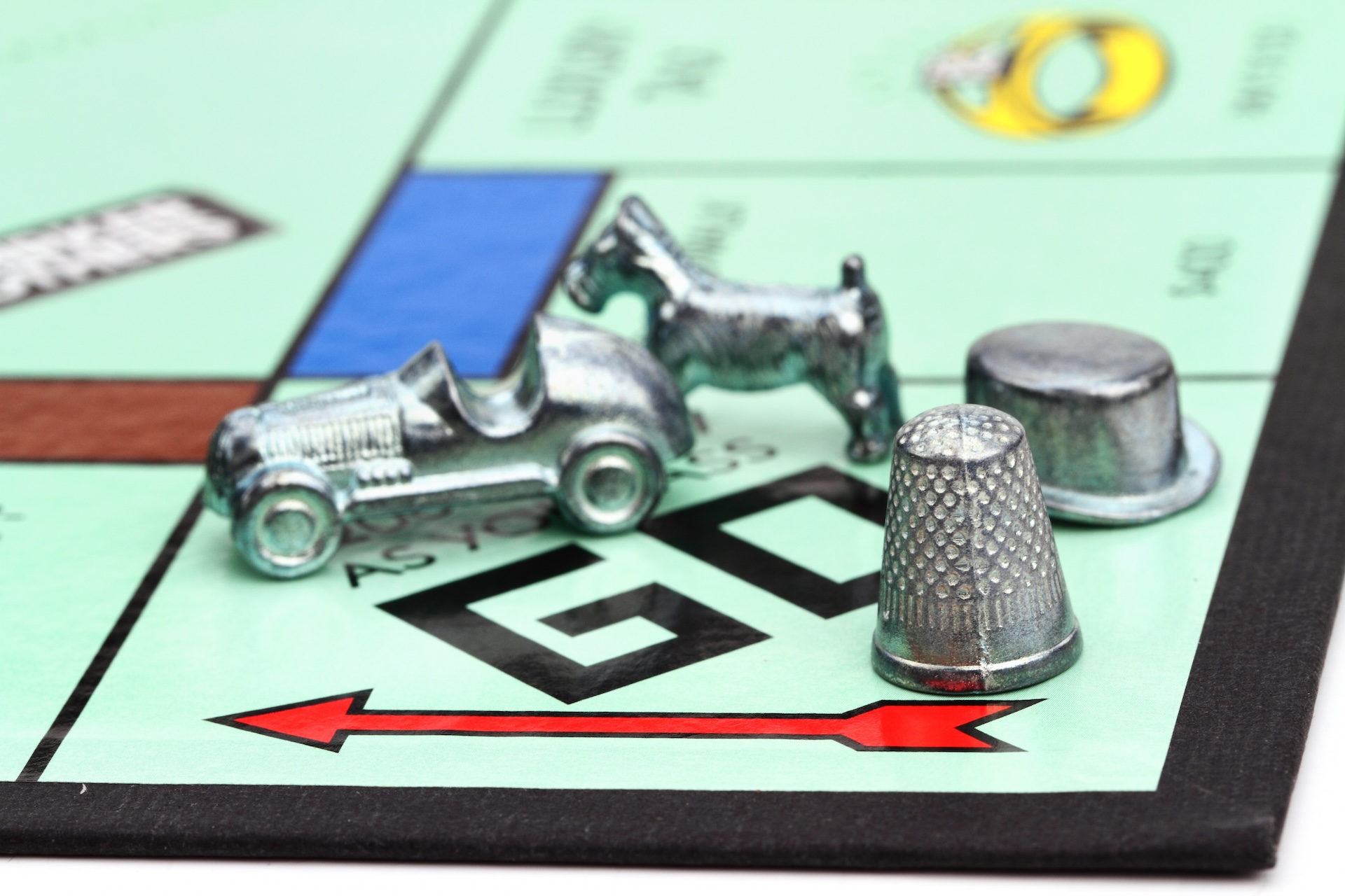 A partial view of a Monopoly game board on a white background showing the Go start square with various game pieces set up on the board