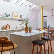kitchen with extension into side return with cream shaker-style cabinets and tongue and groove island, leather stools and suede bar chair on the wall is a neon sign