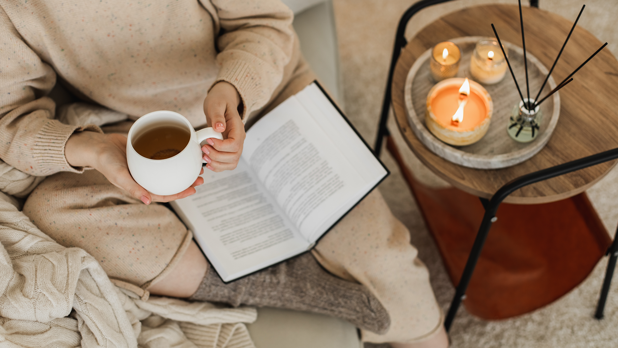 Woman holding a cup of tea and reading a book on a cozy sofa