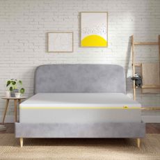 The eveSleep Wunderflip Lighter Hybrid mattress on a grey upholstered bed in a bedroom with a white painted brick wall