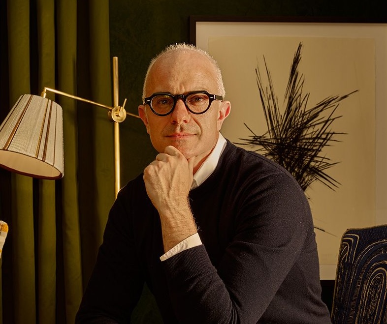 A man wearing glasses and a sweater sits for a portrait.