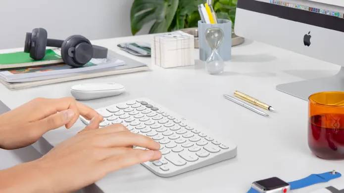 Logitech K380 wireless keyboard in white on white desk in front of an iMac computer