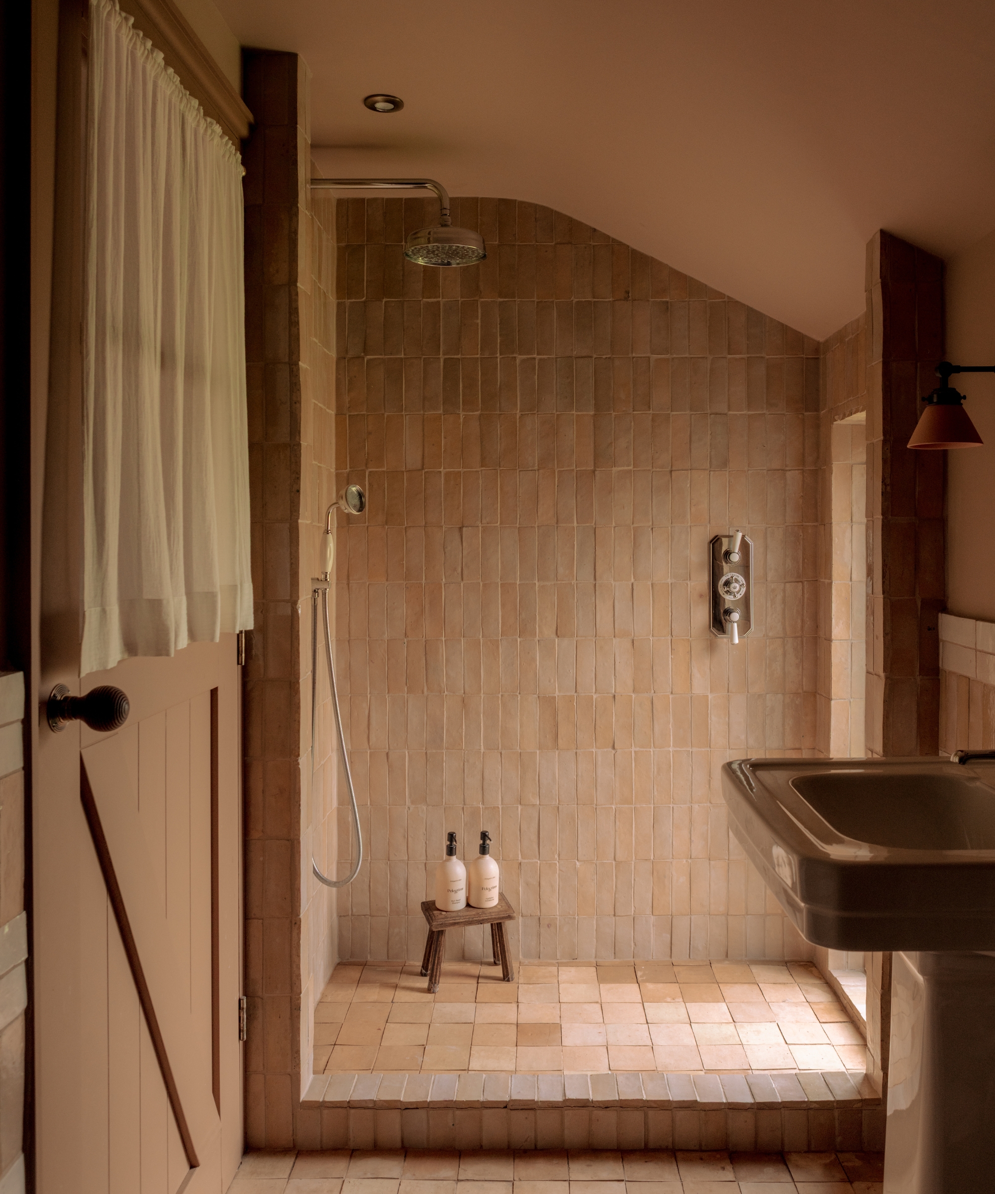 A small loft bathroom with slated ceilings color drenched in soft pink paint, with pink zellige tiles covering the shower area