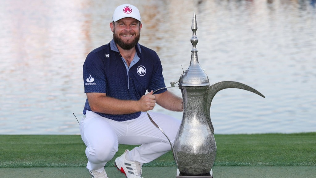 Tyrrell Hatton poses with the Hero Dubai Desert Classic trophy on the 18th green after winning the 2025 tournament.