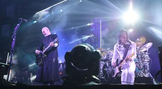 Billy Corgan and James Iha perform onstage with Smashing pumpkins. Corgan wears black and plays a Gibson semi-hollow while Iha wears all white and plays a Strat.