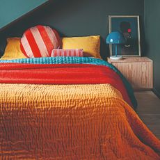 A teal-painted bedroom with a bed covered in throw, pillows and cushions in mustard yellow, orange and red