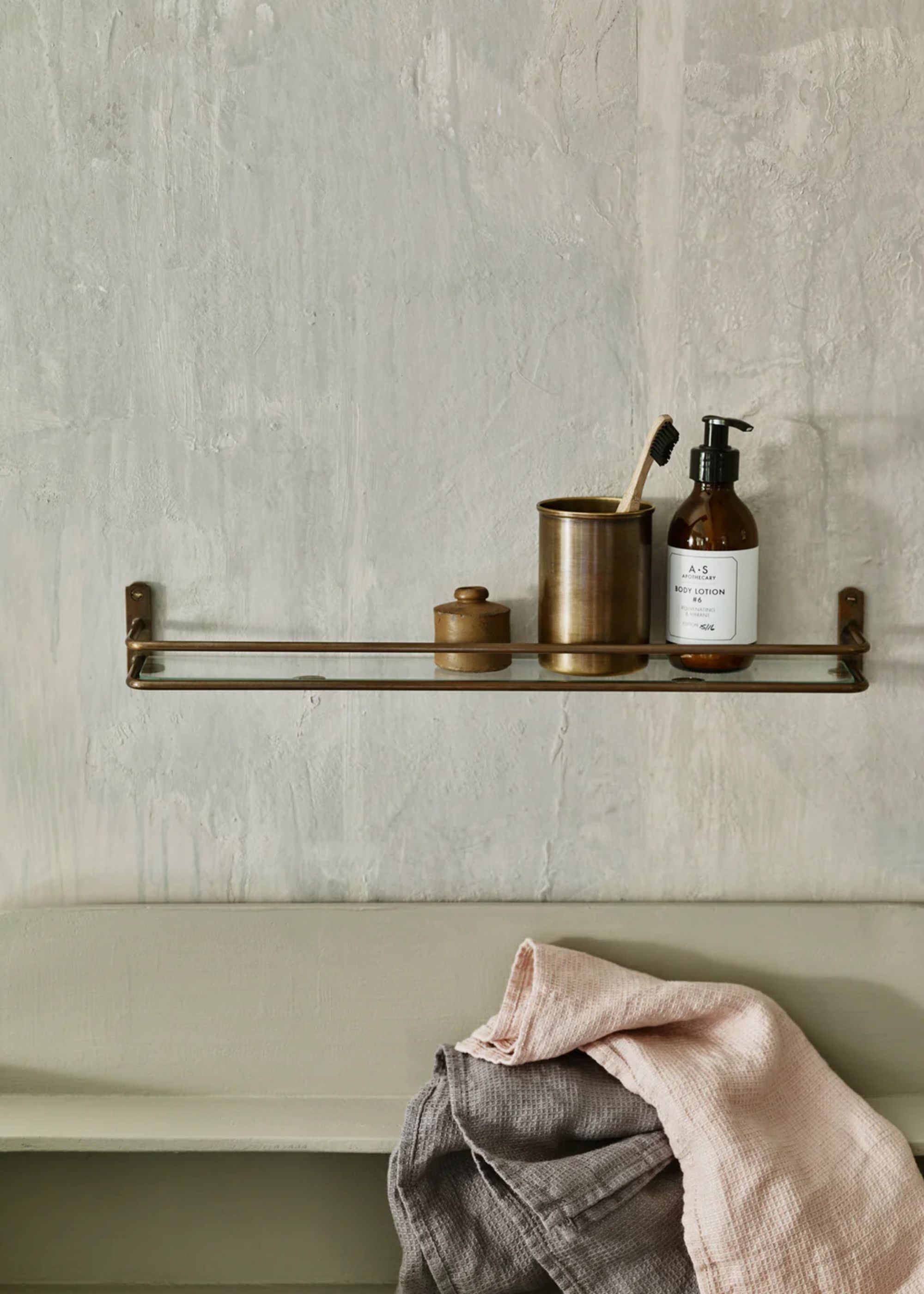 An antique brass bathroom shelf with essentials on top of it such as a toothbrush and holder as well as soap. Below the shelf are some towels.