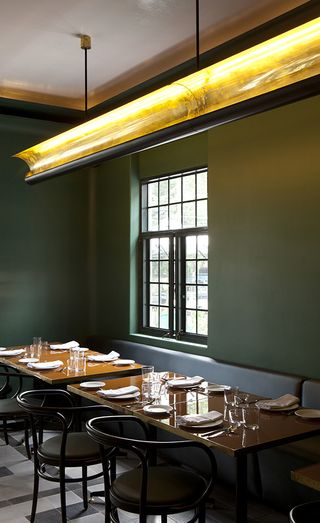 Casa Fayette dining room with green walls, grey floor tiles, long brass ceiling light and black metal dining chairs