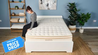 A Tom's Guide mattress tester sat on the edge of the Saatva Classic mattress in a spacious bedroom, with a blue 'price drop' label on top of the image