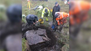 Four men work to excavate a muddy burial site