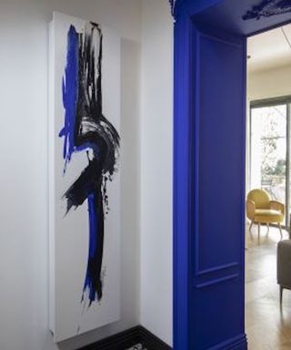 Vertical panel radiator with blue and black paint design by a blue painted doorway