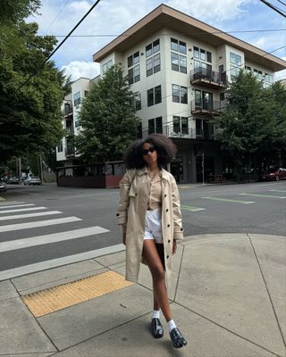 Woman wearing boxer shorts with trench coat and loafers.