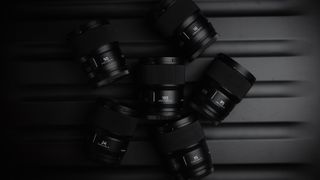 Panasonic Lumix S 100mm f2.8 Macro lens surrounded by other Panasonic lenses in a dark environment